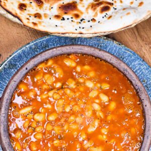 Wiße Bohnen in tomatiger Brühe, gekocht mit Zwiebeln, Peperoni und Gewürzen. Flüssige Konsistenz, serviert im Tontopf.82