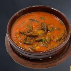 Zarte Okraschoten mit zartem Lammfleisch (400g) in kräftiger Soße mit Tomaten, Zwiebeln, Peperoni und Kräutern gegart. Im Tontopf serviert.'